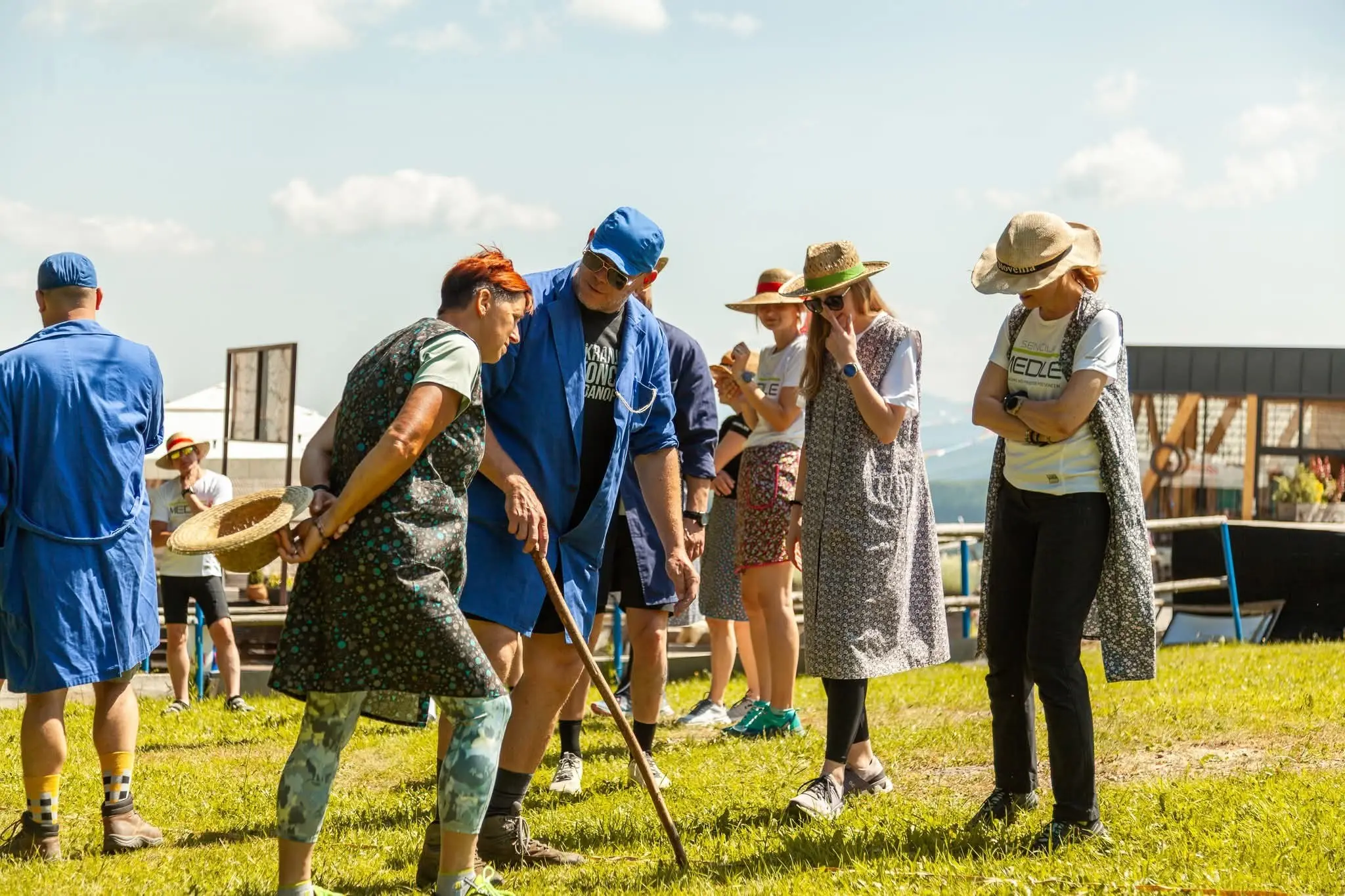 Skupina ljudi, oblečenih v modra in pisana oblačila, na travniku med pogovorom in zabavo na prostem dogodku.