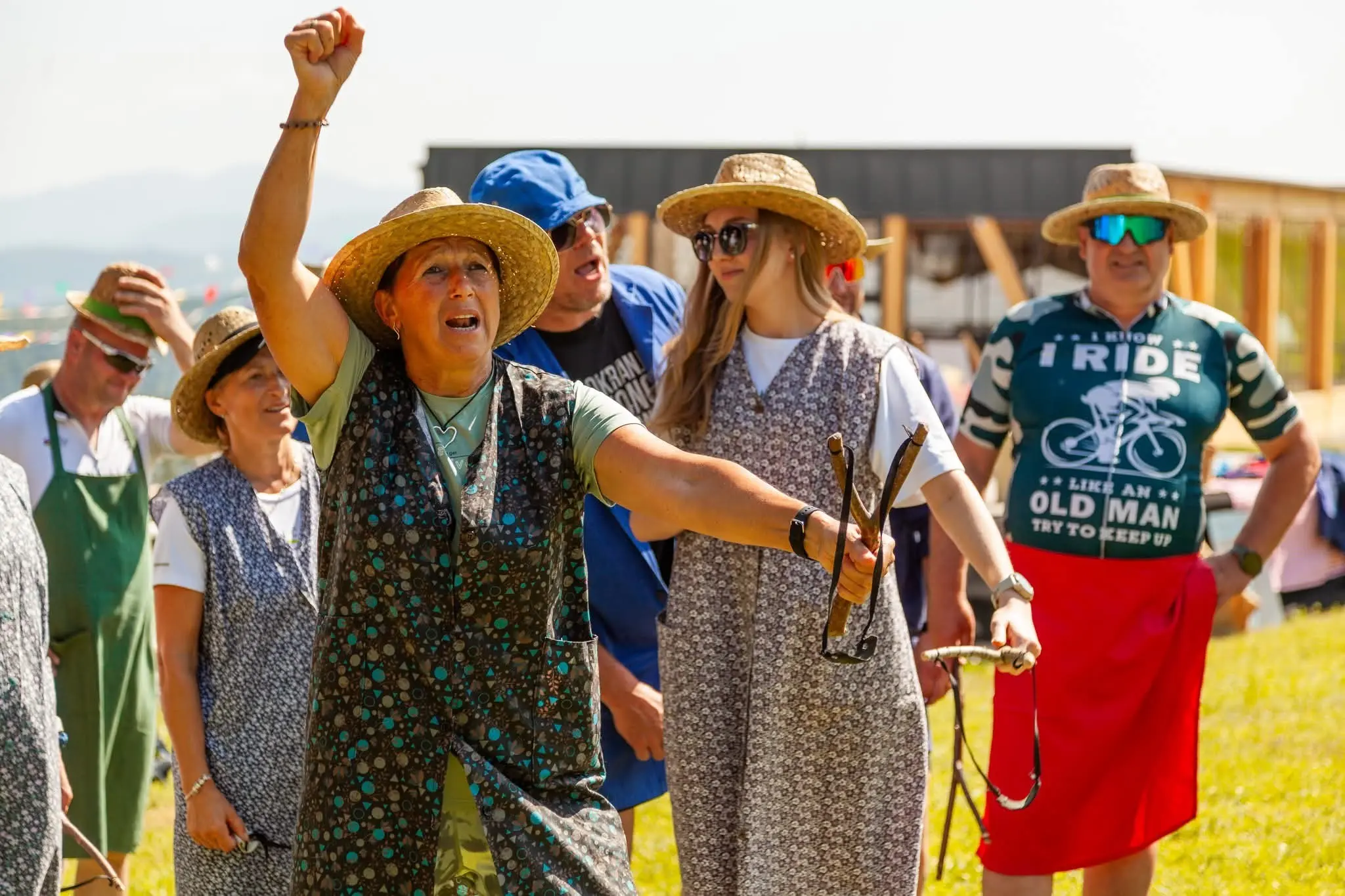 Skupina ljudi na prostem, oblečeni v klobuke in poletne obleke, ki se zabavajo na sončen dan.